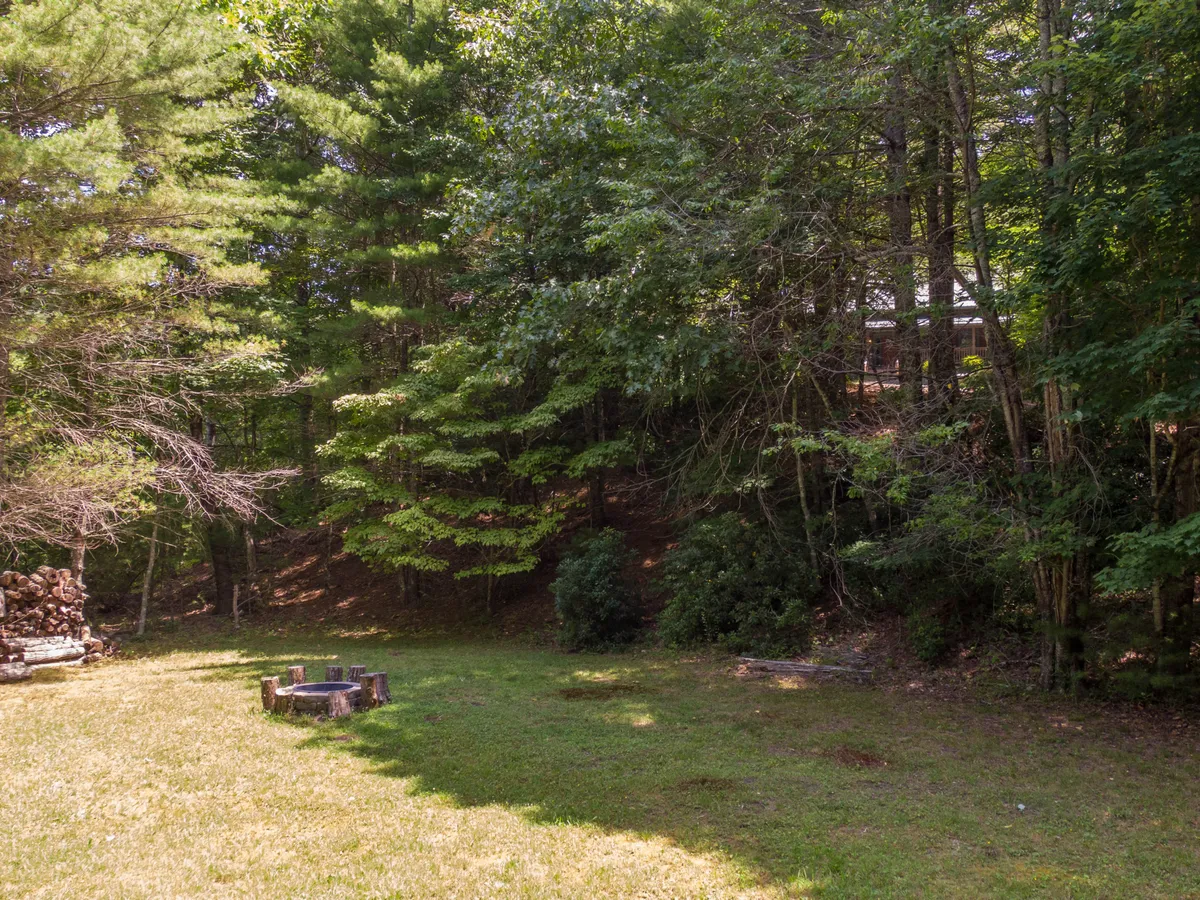 A cozy fire pit set in a grassy clearing surrounded by tall trees, providing the perfect setting for evening gatherings, s'mores, and storytelling under the stars.