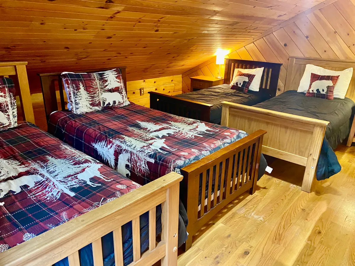 A kid-friendly room featuring four wooden twin beds, each adorned with plaid bedding. The beds are arranged to foster a sense of togetherness, with soft lighting and warm wood walls creating a welcoming, homey vibe.