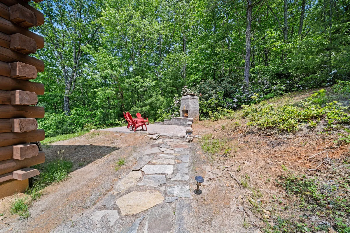 A tranquil outdoor area featuring red Adirondack chairs and a stone pathway leading to an outdoor fireplace, surrounded by lush greenery. The setup invites relaxation, storytelling, and connecting with nature, echoing the diverse seasonal activities available.