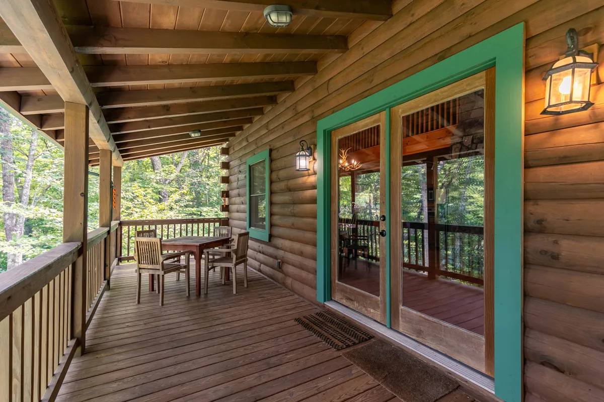 A spacious wooden deck with a large outdoor dining table and inviting glass doors leading inside. Decorative lighting and expansive views of the natural surroundings set the stage for shared meals, stargazing, and tranquil outdoor living.