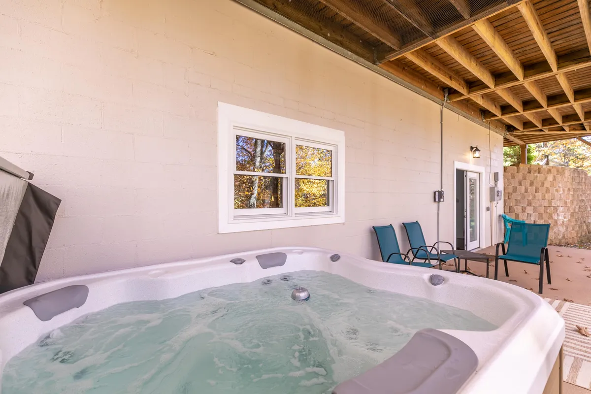 A cozy hot tub surrounded by outdoor seating, adjacent to the cabin with a view through a window. The area is private, inviting guests to relax or take a brainstorming break while enjoying nature.