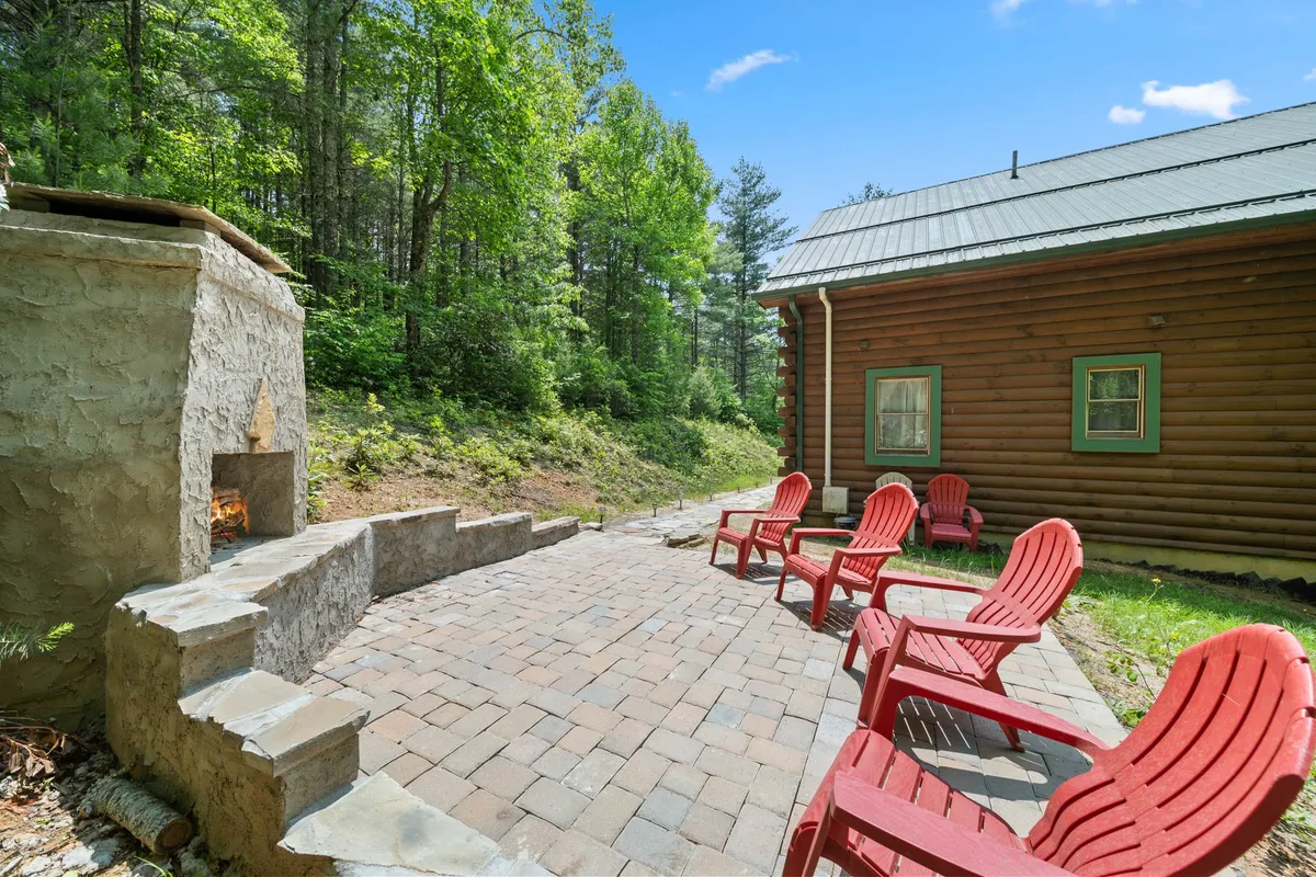 This image features red Adirondack chairs surrounding a stone fire pit beneath green trees. The cozy setup is ideal for relaxing after a day of adventure, stargazing, sharing stories, or sipping hot cocoa on a chilly night.