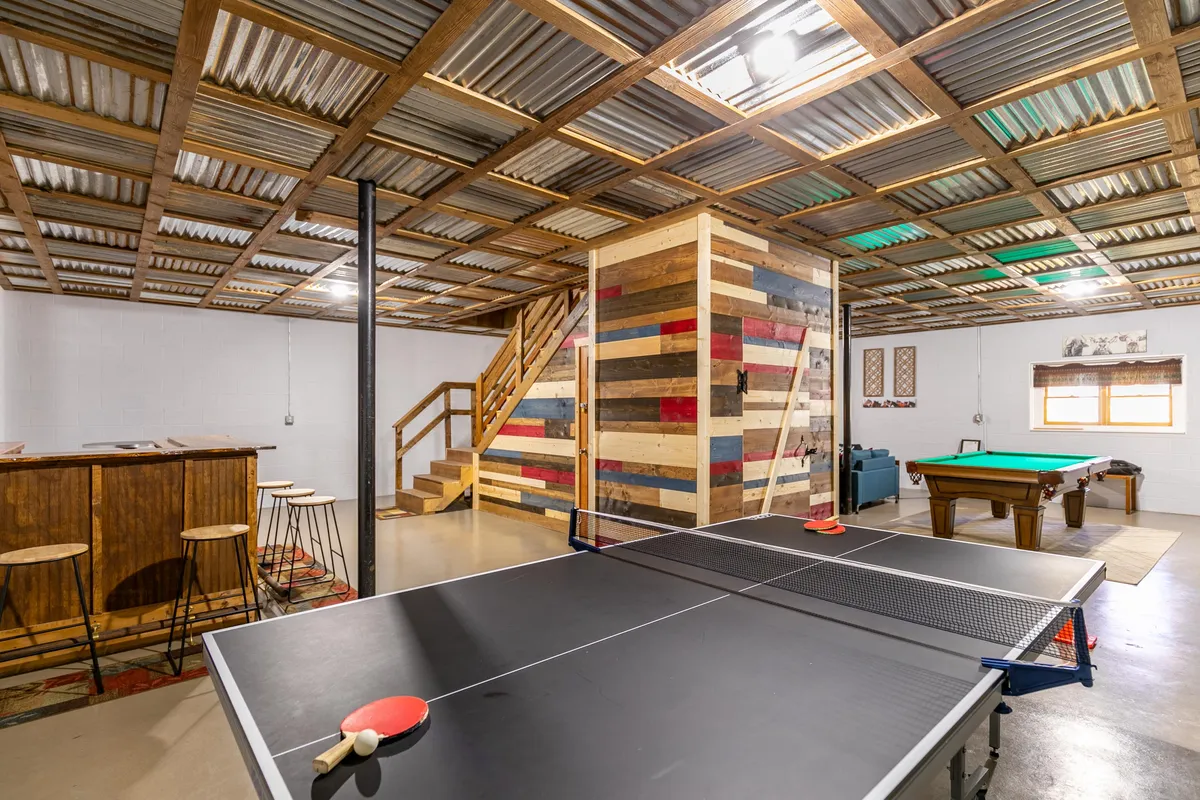 A broad view of the recreation space, featuring both a ping pong table and a pool table, a wooden bar area for refreshments, and a colorful accent wall. The layout encourages group activities and social interaction, with direct connections between gaming and lounging areas.