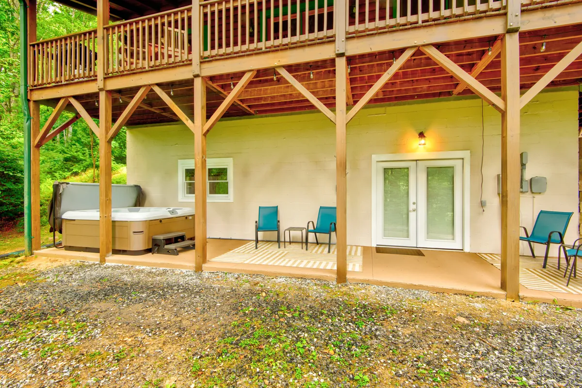 A welcoming patio area with a hot tub, comfortable seating, and double doors opening into the cabin. The setting conveys relaxation after outdoor adventures, stargazing, and socializing in all seasons.
